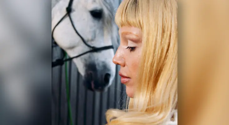 Sam Quealy next to a white horse, a scene from her "Love Lasso" music video which explores the theme of toxic love.