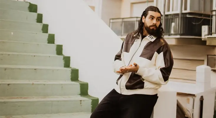 CAMACHO leaning against a white wall wearing a leather jacket to promote his album TEARS IN TORREMOLINOS.