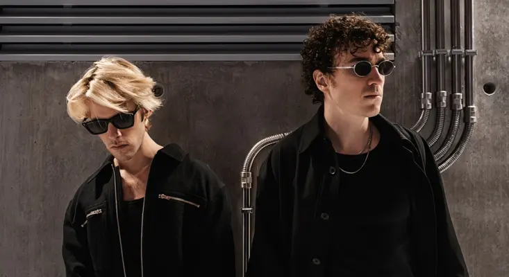 French electronic music duo Ofenbach posing in a concrete industrial setting with sunglasses for their 2026 Miles Away release.