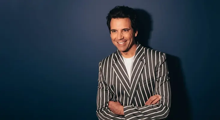 Michael Holbrook Penniman Jr. known as MIKA posing against a navy blue background.