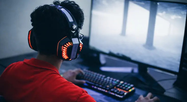 A gamer wearing glowing LED headphones playing a video game on a PC, representing the connection between music and the gaming industry.