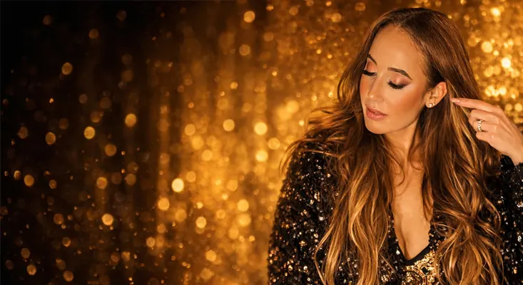 Artist and mother Stefanie Michaela posing in a black sequin outfit against a golden bokeh background.