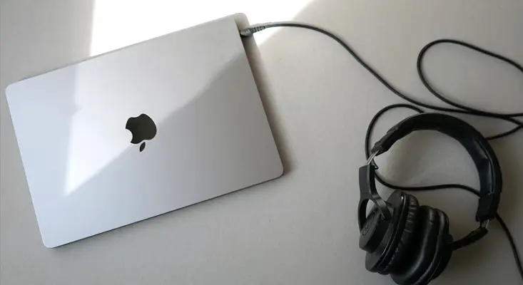 MacBook laptop and DJ headphones side by side representing the best devices for touring DJs playing GameZone Arcade Games.