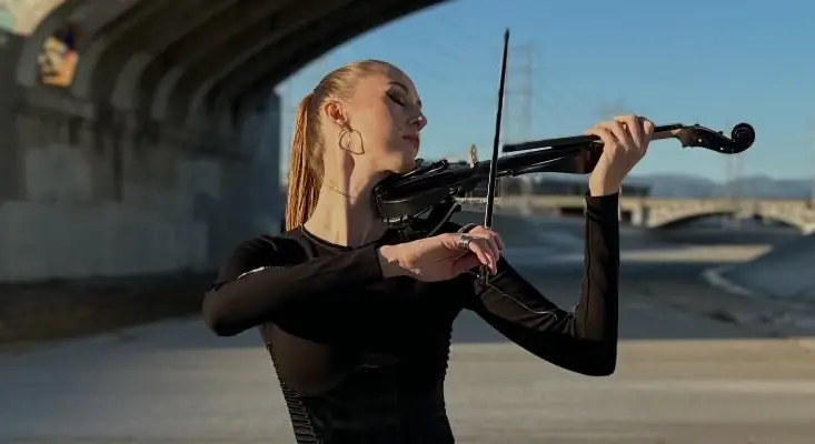 Epic Violin Techno Masterpiece “Vivaldi” By Lila Kova Lila Kova playing a black electric violin outdoors under a bridge for the Vivaldi music video.