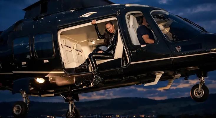 Lilly Palmer sitting inside the open door of the black HB-ZPX luxury helicopter at night during the Bigger Than Techno music video shoot.