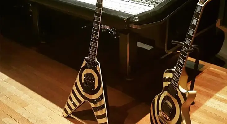 Two Gibson Custom Shop Flying V guitars with black and white Zakk Wylde bullseye design leaning against a road case in a recording studio.