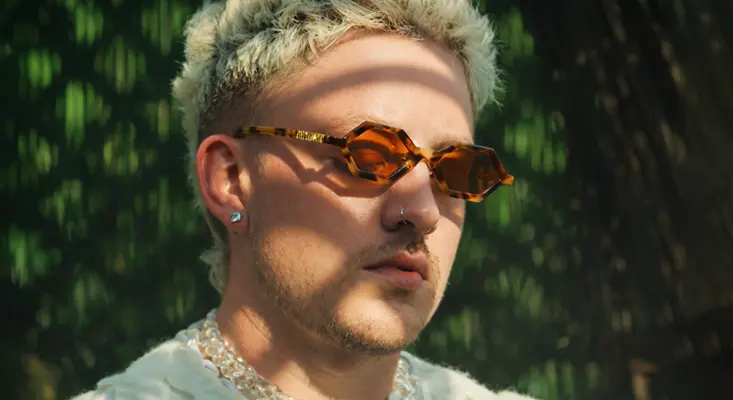 Matt Paris wearing tortoise shell sunglasses and a pearl chain necklace, artist behind the Latin track Santa Marta Colombia.