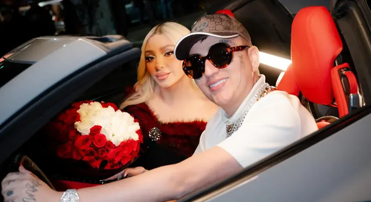 Bellakath and Dani Flow posing in a luxury sports car with a large bouquet of red roses for their "Sin Ti" music video.