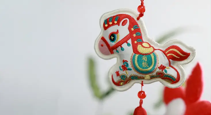Harnessing the vibrant energy of the Fire Horse: Clear out the clutter and refresh your space with our latest Electro-Pop playlist. A decorative white and red embroidered Horse charm for the Year of the Fire Horse, representing energy clearing and Feng Shui for 2026.