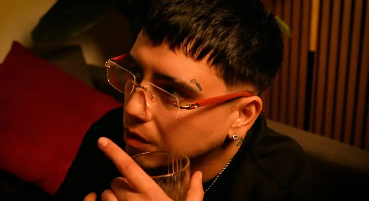 J Francis holding a glass in a moody, dimly lit scene from his urban Latino music video LA GATA.