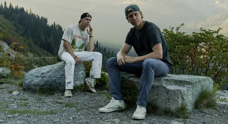MC4D twin DJs and producers Matt and Chris Drake sitting on rocks in a mountain setting.