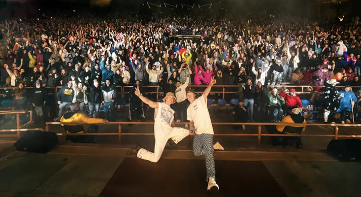 MC4D twin DJs Matt and Chris Drake jumping on stage in front of a large crowd during a high energy live EDM show.