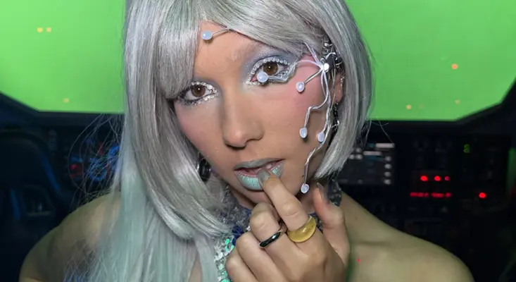 Sophie Grey in futuristic makeup with circuit-like face decorations and silver hair, inside a spaceship set for her sci-fi music video "Cyberspace."