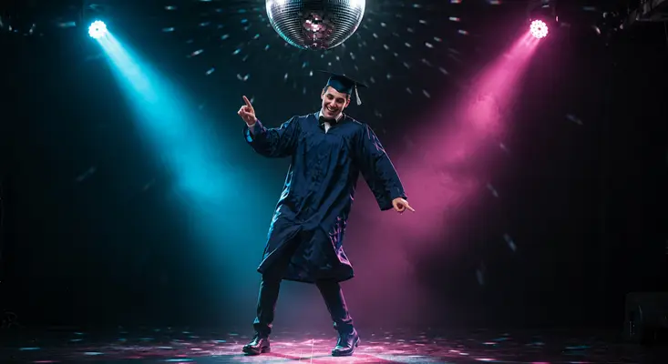 Graduate in cap and gown dancing under disco ball with blue and pink stage lights at graduation party.