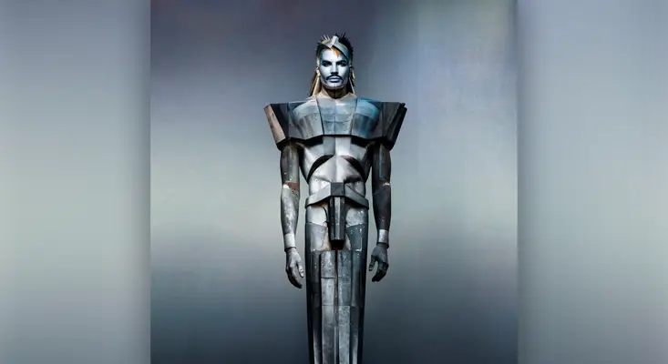 Adam Lambert - UNDER THE RHYTHM Adam Lambert sporting futuristic metallic armor with sharp shoulder pads and silver face paint for the Under the Rhythm single cover art.