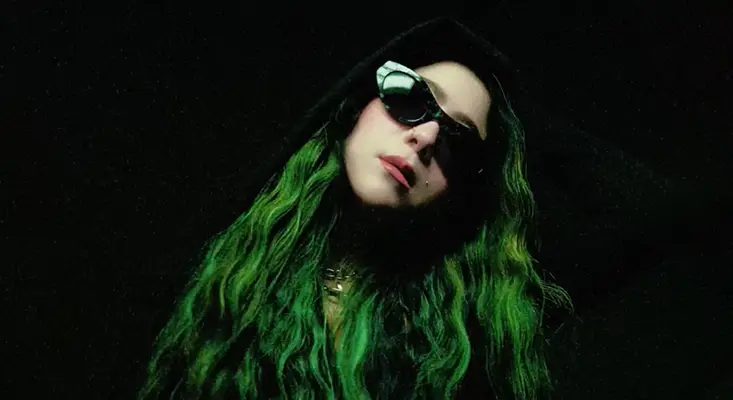 Hard Techno Loud And Unfiltered: RayRay's “My Way” RayRay with green hair and black sunglasses in dark setting for Hard Techno single My Way.
