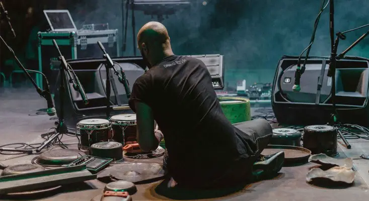 Dario Rossi brings his legendary, high-energy live performance setup to the stage. Italian drummer Dario Rossi performing live on stage surrounded by electronic gear and recycled percussion elements.