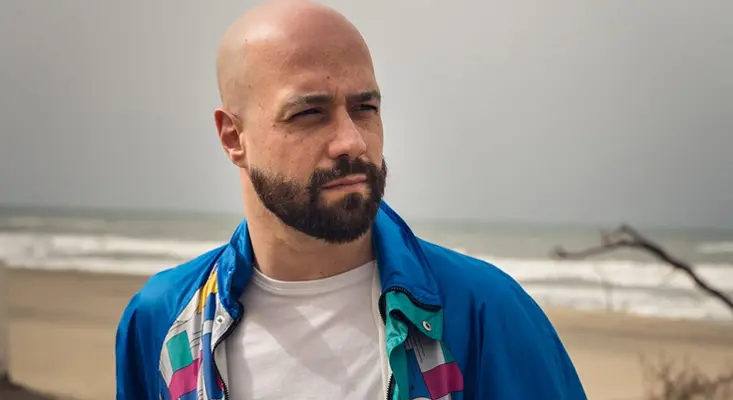 Dario Rossi Recalls 80s New Wave Bands On “We’ll Meet Again” Dario Rossi wearing a retro jacket on a beach, channeling the sound of classic New Wave bands.