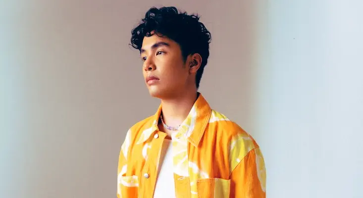 From TikTok Covers To Original Songs: The Rise Of Rakhano Rakhano looking thoughtfully to the side, wearing a vibrant orange and yellow patterned jacket.