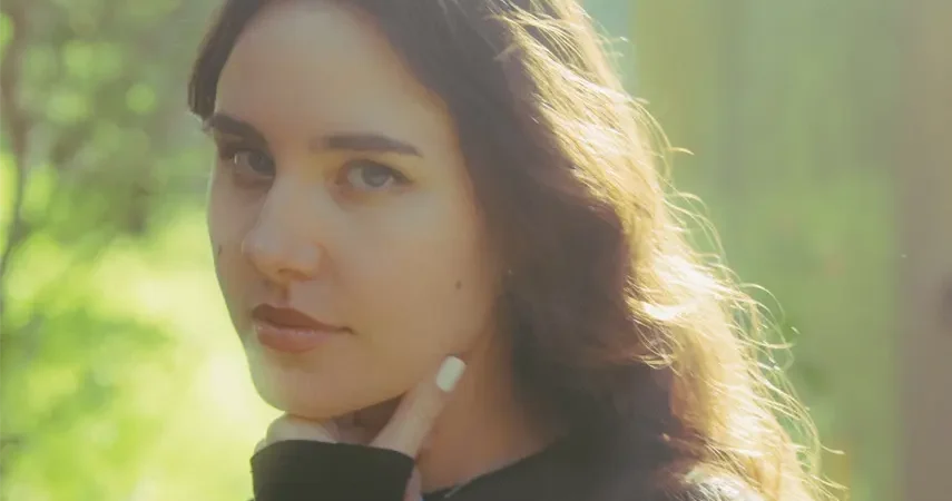 Close-up portrait of electronic music producer Pretty Girl looking at the camera with a soft sun flare background, promoting her Body Step EP.