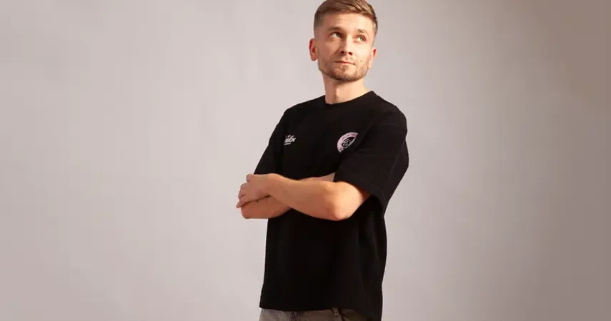 R. Dabizha poses with arms crossed in black t-shirt for Talia interview.