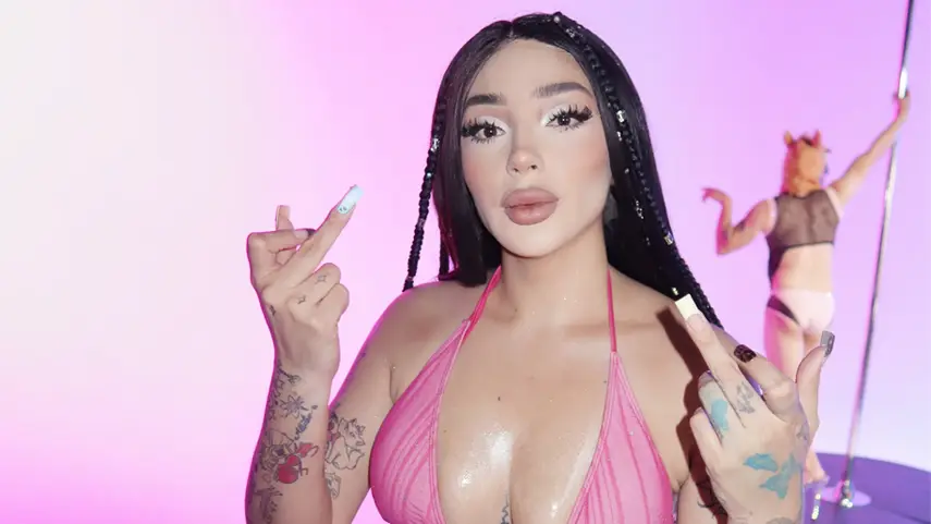 Bellakath holding up middle fingers in a pink top from the CRITICÓN music video, a good song for haters.