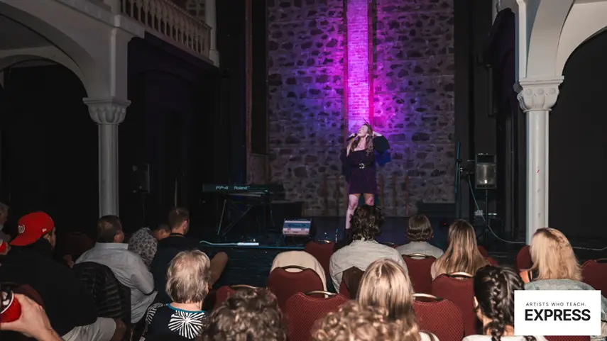 A performer takes the stage at an Express Voice Studio student concert. Singer performing on stage at an Express Voice Studio concert with a live audience.