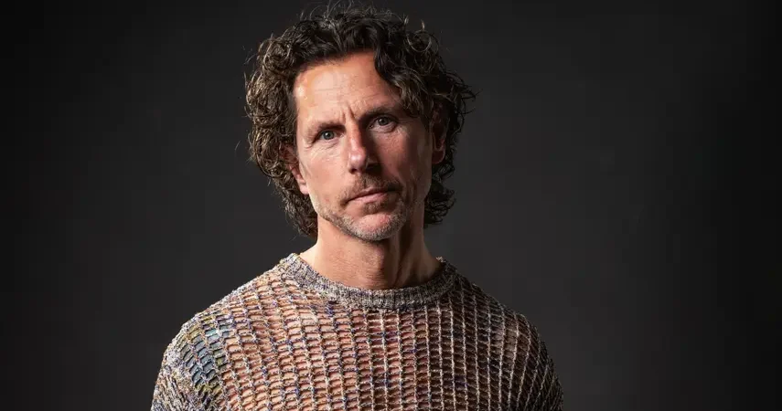 Afro House DJ and producer Kevin Kinembe in a studio portrait, wearing a knit sweater against a dark background.