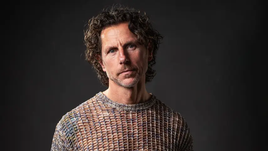 Afro House DJ And Producer Kevin Kinembe Dives Into “Dunda” Afro House DJ and producer Kevin Kinembe in a studio portrait, wearing a knit sweater against a dark background.