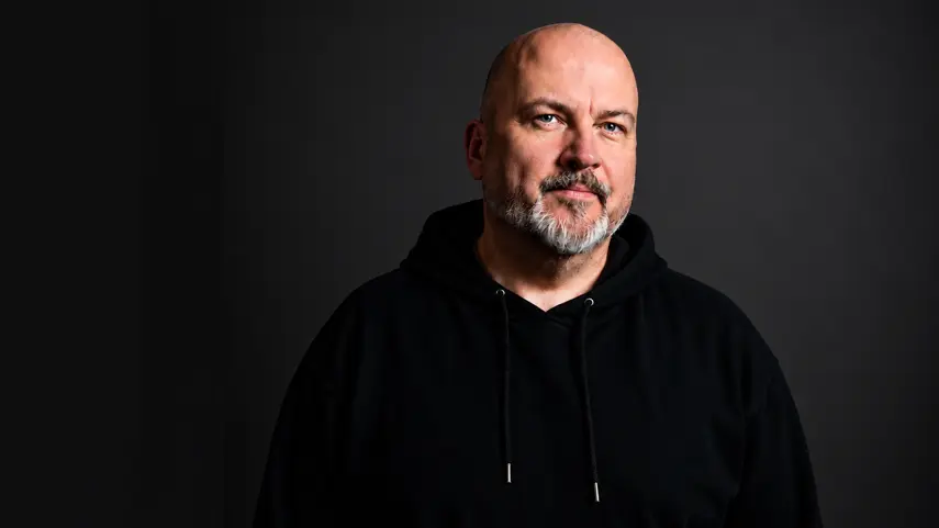 Talla 2XLC, electronic music producer behind the RRAW alias, in a black hoodie studio portrait promoting his Tech Trance single "Angel Mode."