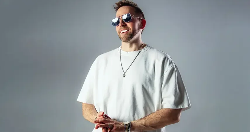 Underground techno DJ Sam Wolfe smiling in white t-shirt and sunglasses.