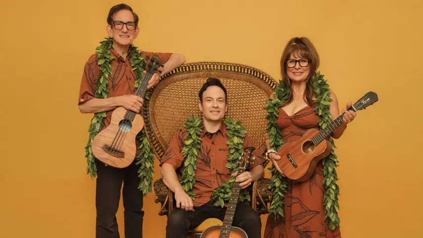Slack Key ʻOhana family trio wearing lei and playing ukulele and guitar.