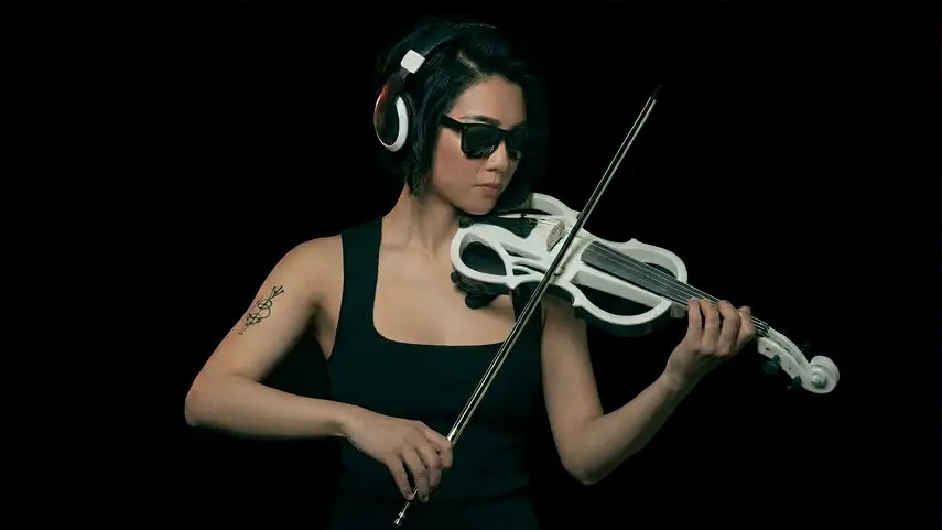 Electric violin in EDM: woman wearing headphones and sunglasses playing a white electric violin against a black background.