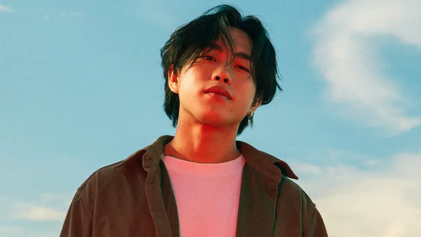 Max Jordan, Indie Pop Artist, Discusses New EP ′Scared To Fall′ Indie pop artist Max Jordan in a brown overshirt and pink tee against a blue sky.
