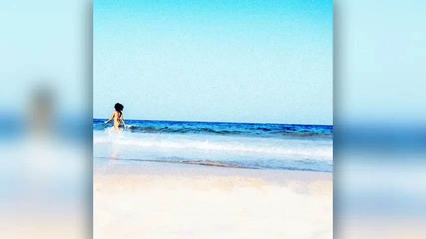 The cover art for Tommy Phillips’ “Sun Is Shining (Lovelee Dae),” a beach scene that matches the summer vibes of the track. Cover art for Tommy Phillips “Sun Is Shining (Lovelee Dae)” showing a person walking into the sea on a sunny beach.